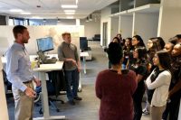 A group of students visiting an IBM office. There are two guys presenting them some slides on a computer screen.