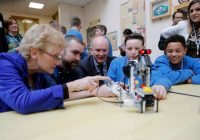 Students, teacher and mentors looking and pointing at a robot created by them.